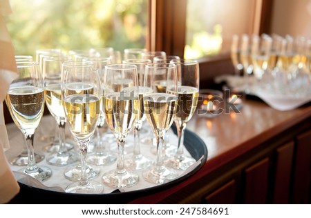 Wedding banquet champagne glasses full of alcohol waiting for bridal guests. Transparent classic glasses with tall stem, objects standing on tray on windowsill, horizontal orientation, nobody.