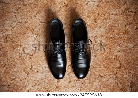 Male dress shoes, elegance wedding groom boots called derby shoes, leather black cloth empty shoes on beige carpet in horizontal orientation, nobody.