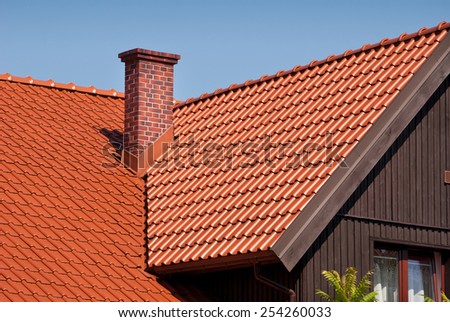 Overlapping red tiles rows sheet roof and chimney, new house building construction of high section in Poland, architecture detail, ridge tiling material regular pattern in horizontal orientation
