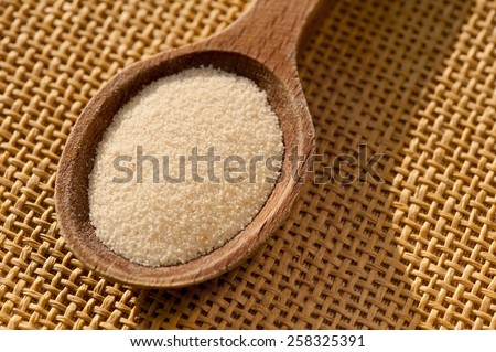 White semolina grains kasha portion on wooden spoon closeup lying on table mat, coarsely grains healthy raw food heap in day light, horizontal orientation, nobody.