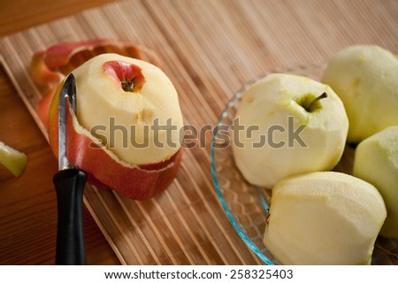 Peeling fresh red apple lying on bamboo mat, black peeler, peelings and whole yellow red healthy fruits on wooden table, nobody, horizontal orientation, view from above.