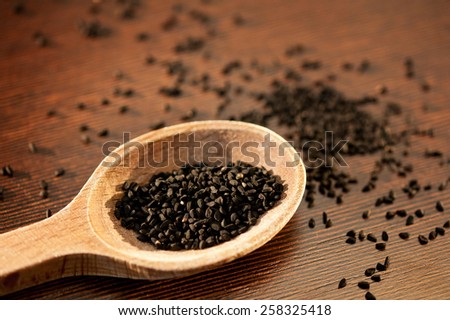 Black whole Nigella Sativa seeds portion on wooden spoon macro, Black cumin raw spice heap in day light, horizontal orientation, nobody. Polish name czarnuszka siewna.