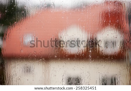 Rainy teary window abstract, house visible through transparent wet rain drops on glass window out of focus, rain flow texture in horizontal orientation, nobody.