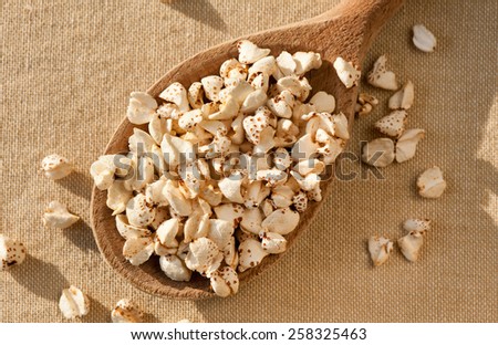 Expanded popped buckwheat groats, puffed crunchy portion on wooden spoon lying on table cloth, grains healthy snack food heap in day light, horizontal orientation, nobody.