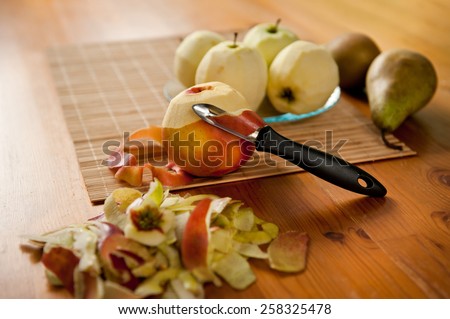 Apples peeling fruits lying on bamboo mat, black peeler, peelings and whole yellow red healthy fruits and green pears on wooden table, nobody, horizontal orientation.