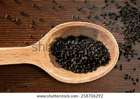 Black whole Nigella Sativa dry seeds portion on wooden spoon macro, Black cumin raw spice heap in day light, horizontal orientation, nobody. Polish name czarnuszka siewna.