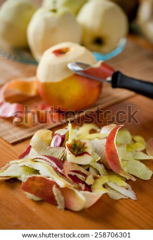 Apple peelings detail, blurred fresh fruit lying on bamboo mat, black peeler, peelings selective focus out of whole yellow red healthy fruit on wooden table, nobody, vertical orientation.
