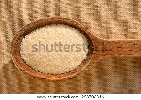 White semolina grains groats portion on wooden spoon closeup lying on table cloth, coarsely grains healthy raw food heap in day light, horizontal orientation, nobody.