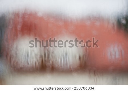 Rainy blurred window abstract, house visible through transparent wet rain drops on glass window out of focus, rain flow texture in horizontal orientation, nobody.