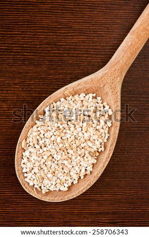 White pearled barley groats portion, coarsely grains portion on wooden spoon lying on dark board closeup, healthy raw food heap in day light, vertical orientation, nobody.