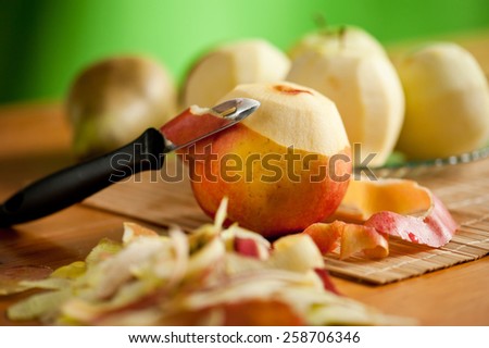 Peeling apples lying on bamboo mat, black peeler, peelings and whole yellow red healthy fruits on wooden table, nobody, horizontal orientation.