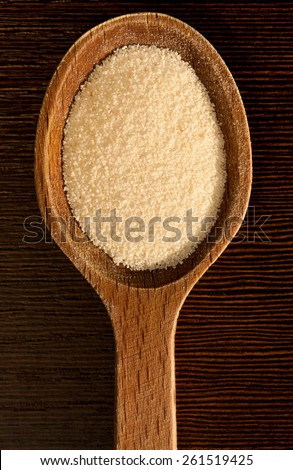White semolina grains pile portion on wooden spoon closeup lying on dark board, coarsely grains healthy raw food heap in day light, vertical orientation, nobody.