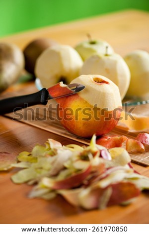 Peeling apple detail fresh fruit lying on bamboo mat, black peeler, peelings and whole yellow red healthy fruits on wooden table, nobody, vertical orientation.