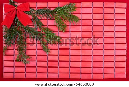 Fresh green spruce twig with red bow lying on red bamboo mat sheet in horizontal orientation.