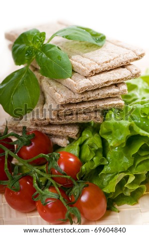 Pile of dry crisp bread slices with cherry tomato and basil green leaves on lettuce leaf, food staple of diet products in vertical orientation, nobody.