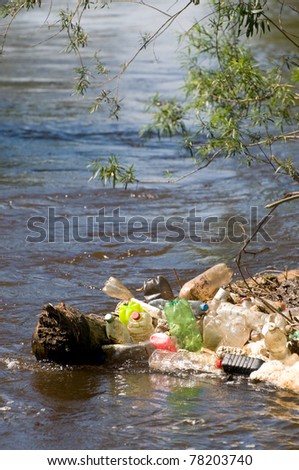 Coast and garbage plastic bottles damage river after flood in Poland. Scatter empty plastic bottles stuck on log in water under small twigs of bush, dump environment, objects spilled out, vertical