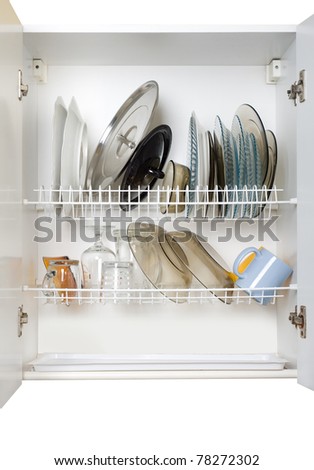 White dish draining closet with wet dishes of glass and ceramic, plates, bowls, covers and mugs fragile objects drying inside on rack made of plastic coated steel wire and open bottom, open doors