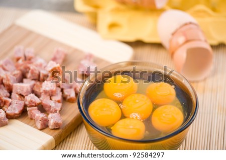 Six raw egg yolks in glass bowl and cut sausage lying on board, preparing scramble eggs, horizontal orientation, nobody, objects in studio shot.