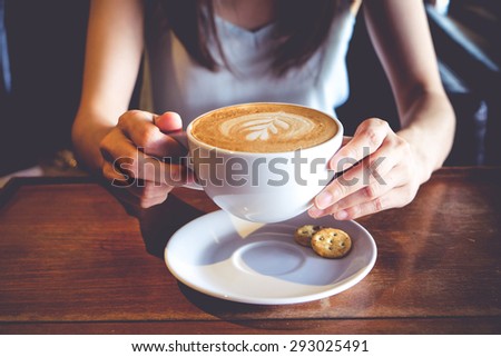 women hold a cup of latte art coffee on wood table, latte art