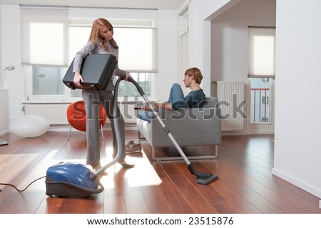 Business woman is vacuum cleaning while the lazy boyfriend is sitting on the couch watching tv