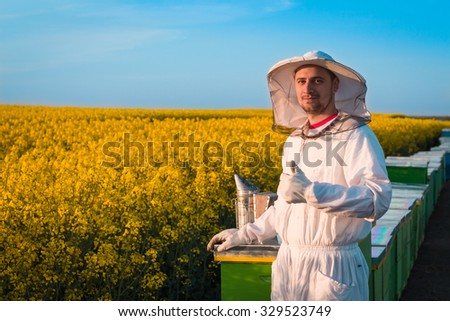 Happy young beekeeper working in the field of yellow flowers