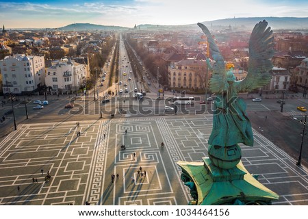 Budapest, Hungary - Angel sculpture from behind on the top of Heroes\' Square at sunset with Andrassy street and the skyline of Budapest at background