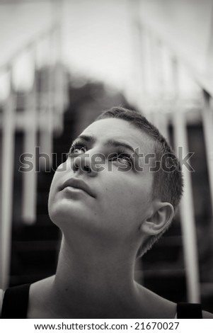 Close-up black-and-white portrait of a beautful teenager girl looking upside and thinking. Stairs on the background