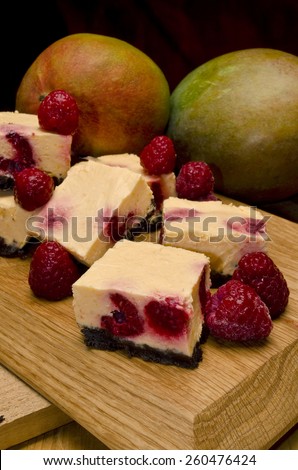 some dessert squares made of mango puree with raspberry in it on a chocolate cookies crumble crust, presented on a wood cutting board with fresh raspberry as decoration