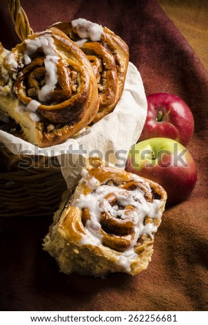 a wicker basket layered with an off-white cloth is filled with some chelsea apple brioche with two brioches place on the side of the basket, shot on a medium brown backdrop