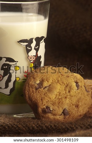 close-up shot of some chocolate chip cookies lying on a small glass of milk printed with a cow drawing,