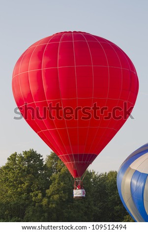 SEYMOUR, WI - AUGUST 3: A red hot air balloon is just lifting off the ground next to another balloon at the Balloon Rally at the Annual Hamburger Festival on August 3, 2012 in Seymour, Wisconsin.