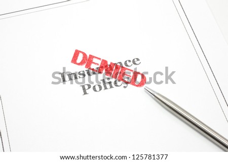 An insurance policy and a pen and the word Denied in red stamp across the policy.