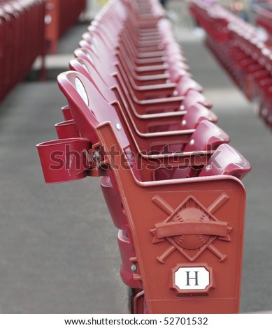 A red stadium seat in detail with rows of seats blurred behind the main seat at a baseball stadium.