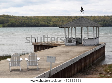 An old weathered private empty dock on Lake Michigan with two chairs and gazebo showing a peaceful scene overlooking the water.