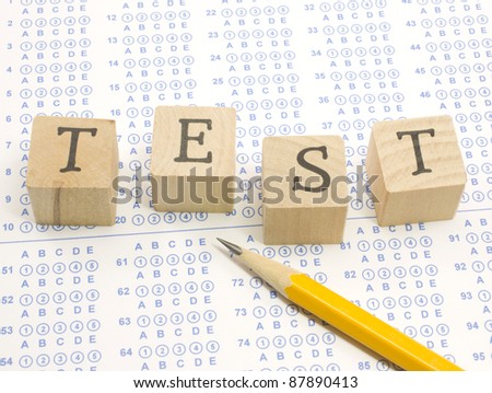 Wooden blocks spell out TEST on a blue bubble or scantron sheet with a number two yellow pencil.