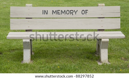 A park bench in the green grass with the words In Memory Of on the top planks with the bottom planks ready for your text.