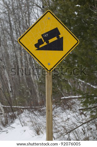 A yellow square or diamond steep hill truck incline sign against a winter forest.