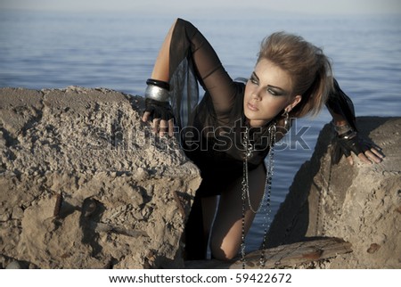 A beautiful young girl dressed in a biker on a concrete slab on a background of water