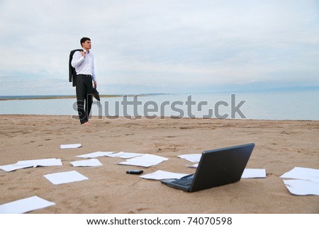 A young businessman walking on the beach. On the sand scattered papers, laptop and mobile phone.