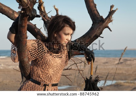 Beautiful young girl with a black umbrella is based on the tree. Background sandy beach.