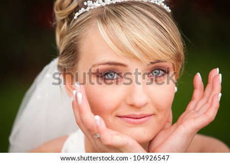 portrait of blond haired young pretty bride with crystal blue eyes and diadem and hands besides her face with perfect make-up