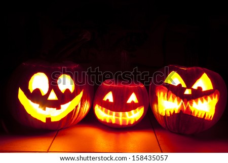 one friendly and two scary pumpkin are shining in scary light in the dark room. three pumpkins on the floor