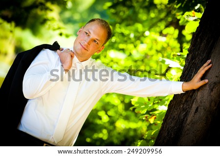 confident groom leaning against tree - groom