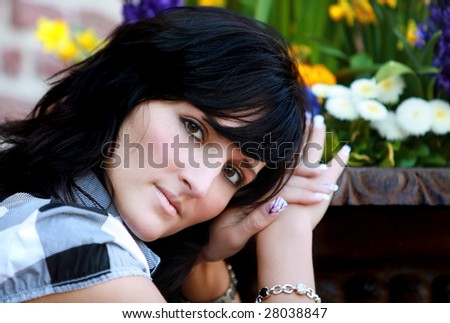 Very nice black haired girl with perfect brown eyes is sitting beside the flower. The flowers are very colorful in the spring time.
