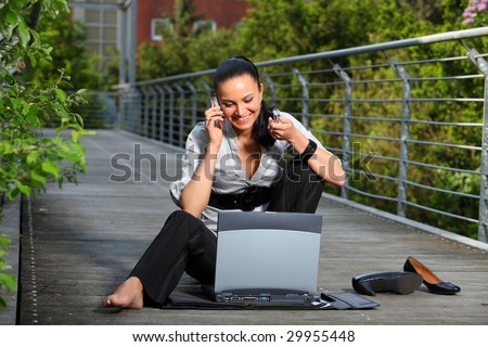 Business Woman sitting down on the ground with laptop and cell phone barefeet.