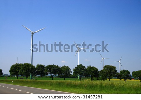 Photo shows the new wind energy machines in germany. blue sky little clouds and nice fields. a street besides the field.