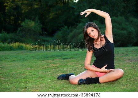Sports girl is laying down on a meadow and enjoys her training. it is a mix of yoga, meditation and gymnastics. she is very pretty and a young lady.