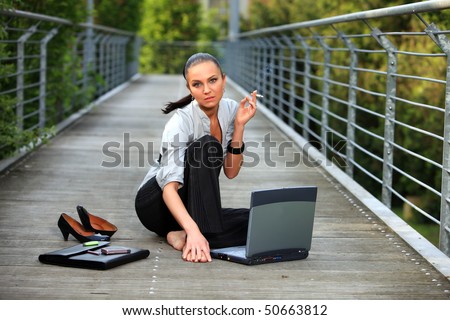 pigtailed smoking business lady with laptop relaxes her cigarette break and sitting on the outdoor summer ground