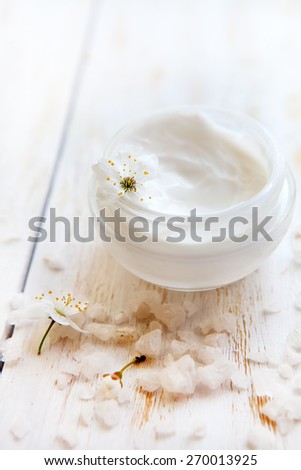 Pot of beauty cream surrounded by flowers  on white wooden table