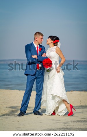 The groom and the bride on a beach (a red bouquet, a red tie, red shoes)